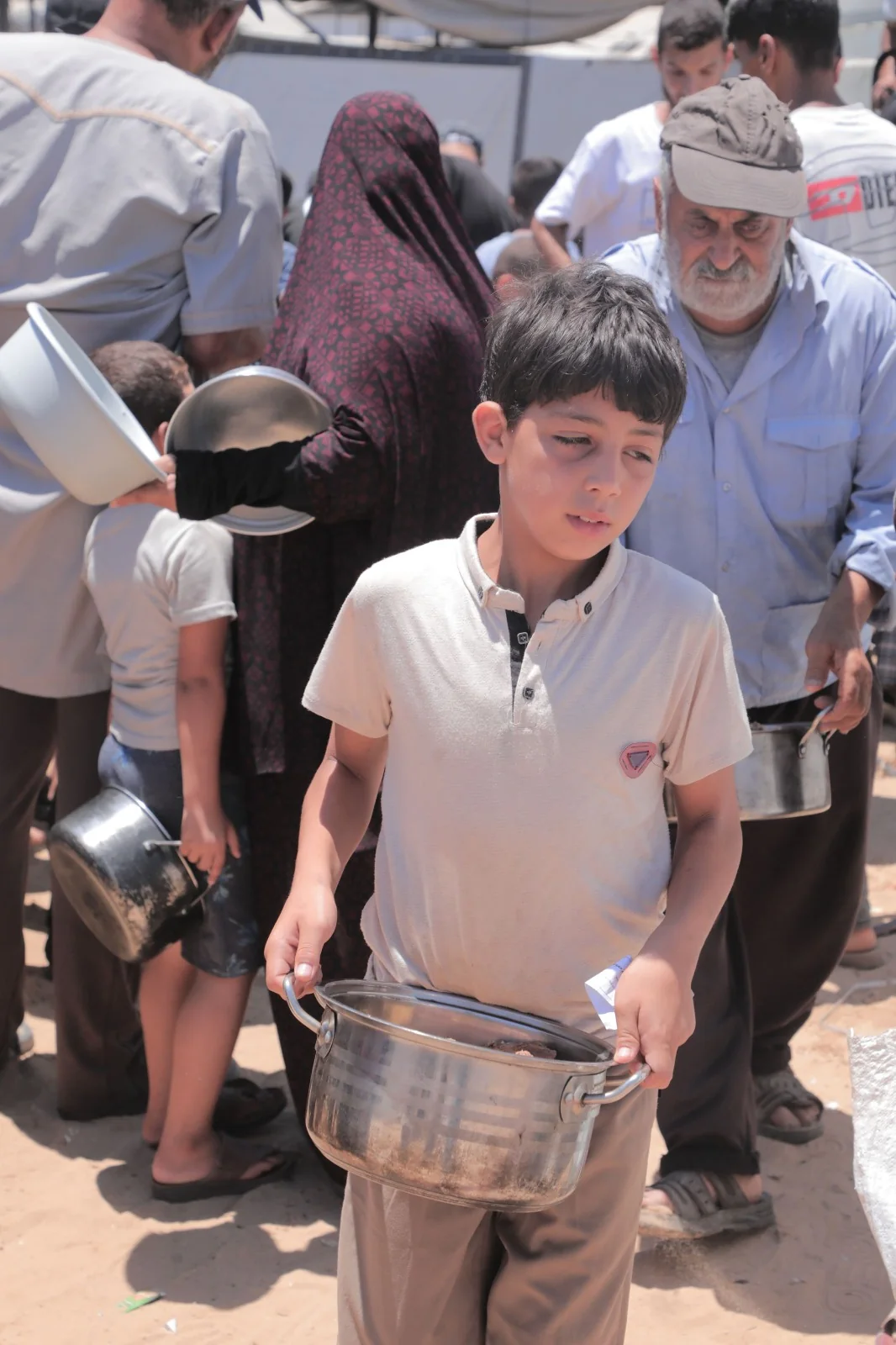 A boy carrying a cooking pot through a crowded aid distribution