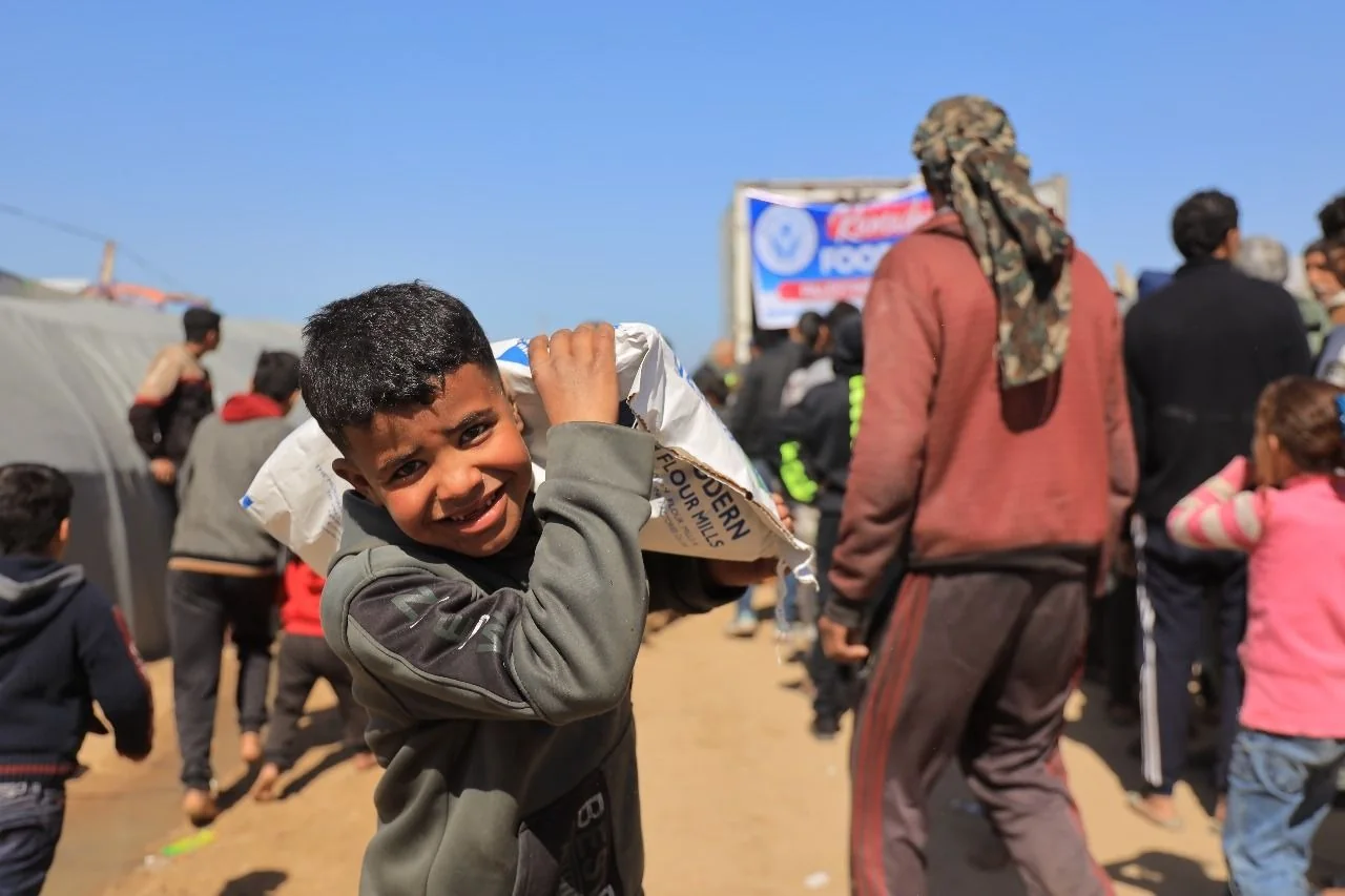 A child carrying a bag of flour through a crowded area