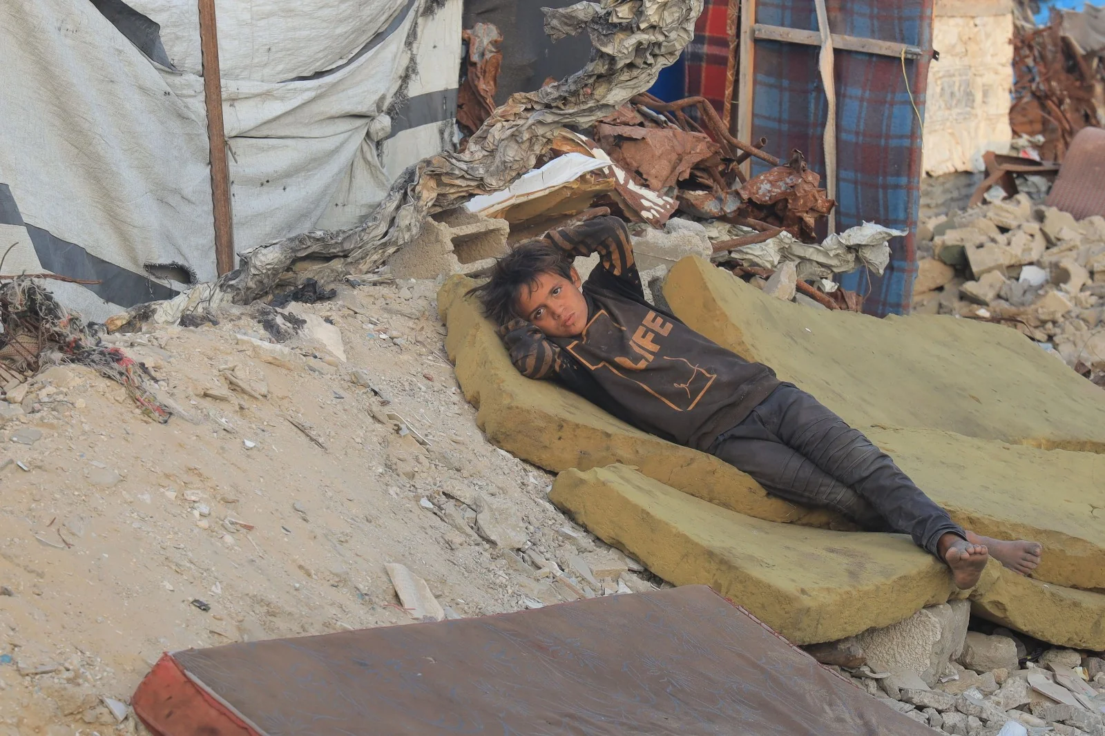 A displaced child resting outside a temporary shelter