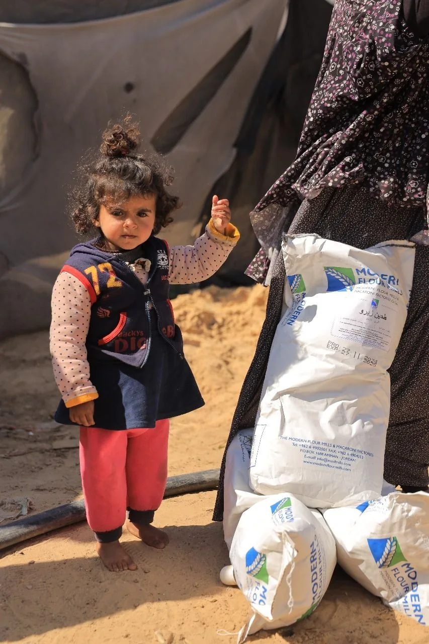 A young girl standing beside bags of relief supplies